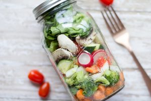 salad in a glass jar with a lid. Cherry tomatoes and a fork next to it.