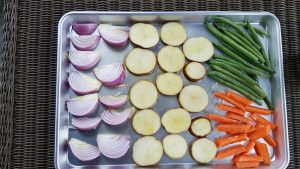 image of sliced potatoes, onions, carrots and green beans on a cookie sheet for a buddha bowl from intentionally eat