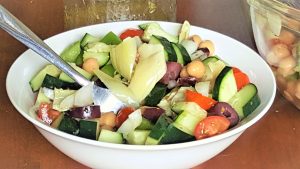 image of tangy greek chickpea salad in a white bowl. a fork is in the bowl.