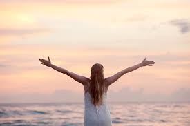 image of a woman with her back to the camera looking at the ocean with outstretched arms. freedom from overeating by intentionally eat