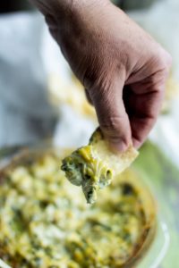 image of healthy spinach artichoke dip by intentionally eat with cindy newland with a hand dipping a chip