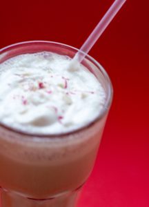 image of a glass full of Skinny Peppermint Vanilla Protein Shake by Intentionally Eat with a straw and a red background