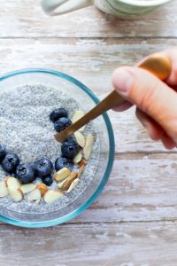 image of easy chia seed pudding by intentionally eat with blueberries, slivered almonds and a hand holding a spoon
