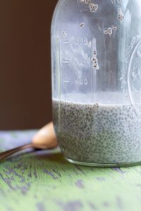 image of easy chia seed pudding by intentionally eat in a jar with a spoon next to it on a green wooden table