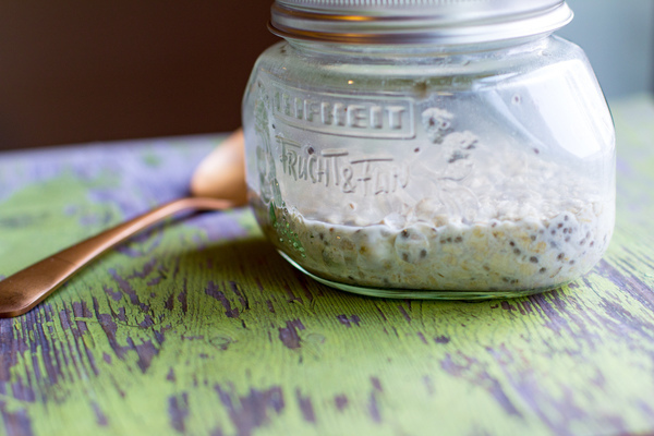 image of simple overnight oats by intentionally eat in a glass jar with a metal lid and a copper spoon on a green wooden table