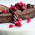 image of 125 Calorie Flourless Chocolate Cake by intentionally eat with a fork cutting through the cake and the cake is covered in pomegranate seeds