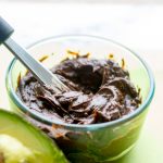 image of chocolate avocado frosting in a clear glass dish with a knife and an avocado next to the dish