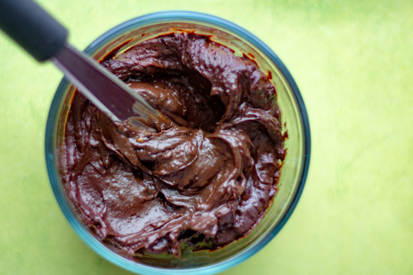 image of chocolate avocado frosting by intentionally eat in a clear glass bowl with a spatula