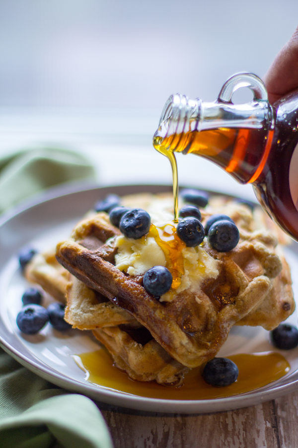 image of perfect protein waffles by intentionally eat with maple syrup being poured over waffles covered in blueberries