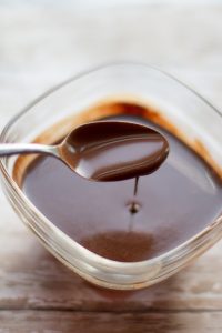 image of easy dairy free hot fudge sauce by cindy newland with intentionally eat in a glass bowl with a silver spoon full of hot fudge 