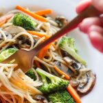 image of Easy Vegetable Lo Mein by Intentionally Eat with Cindy Newland in a white bowl with a hand holding a fork twirling noodles