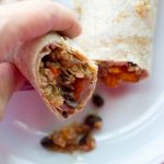 image of Quinoa Sweet Potato and Black Bean Burritos by Intentionally Eat with Cindy Newland with a hand holding half a burrito