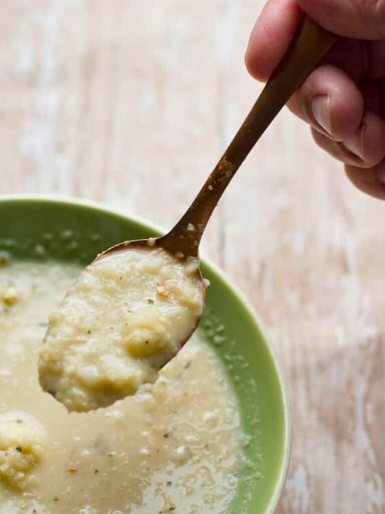 a hand holding a spoonful of cauliflower soup