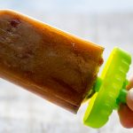 Skinny Caramel Coffee Popsicles by Cindy Newland with Intentionally Eat on a green stick with a hand holding it