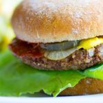 image of Porcini Pecan Vegan Burgers by Intentionally Eat with Cindy Newland with lettuce, onion, pickle, mustard and ketchup on a bun