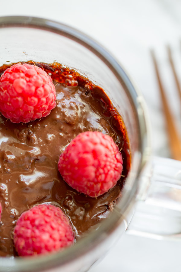 image of Wacky Chocolate Mug Cake by Intentionally Eat with Cindy Newland in a clear mug with a gold fork and raspberries