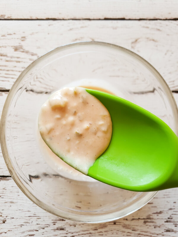 photo of a green spoon full of vegan big mac sauce being held over a glass bowl