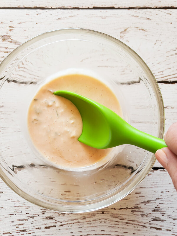 photo of vegan big mac sauce in a glass bowl being stirred with a green spoon