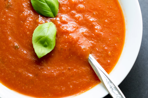 Vegan tomato soup in a white bowl with a spoon and basil leaves