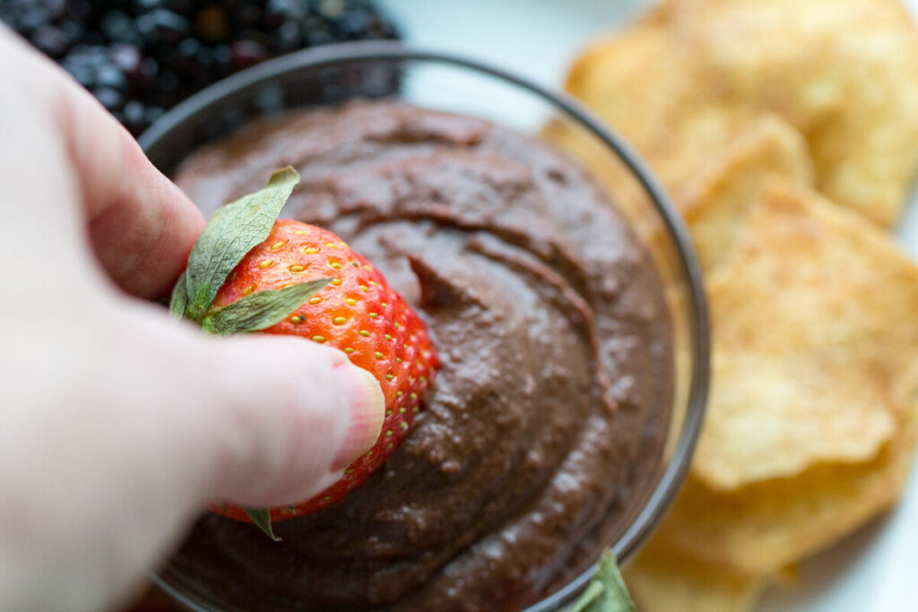 brownie vegan fruit dip with a hand dipping a strawberry