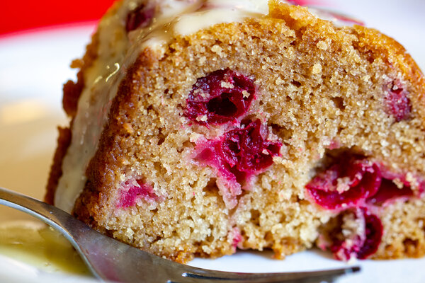 Image of vegan cranberry bliss cake by intentionally eat with cindy newland on a white plate with a fork and cranberries.