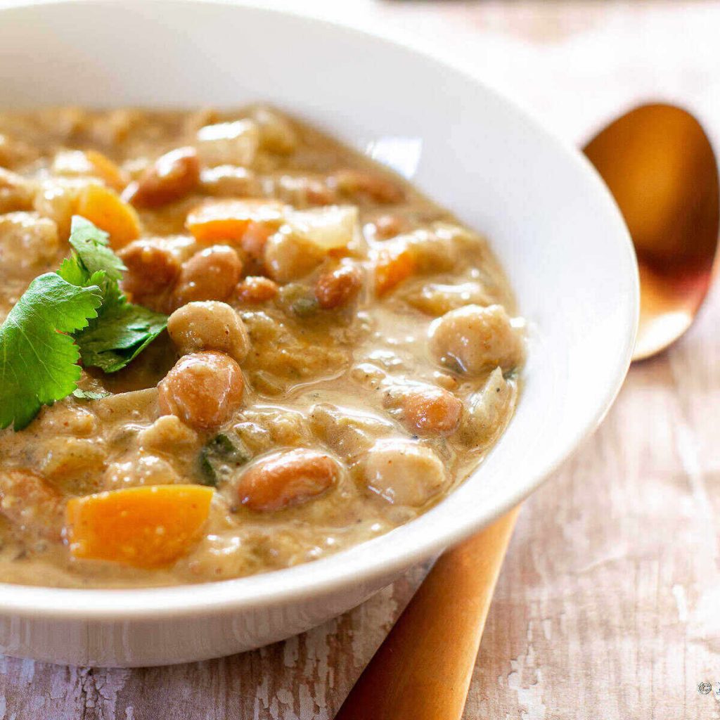image of best vegan white chili in a white bowl with a gold spoon