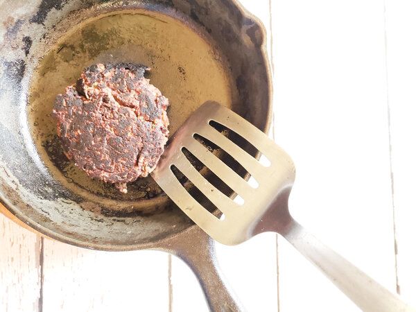 photo of black bean burger in a cast iron skillet being flipped with a spatula