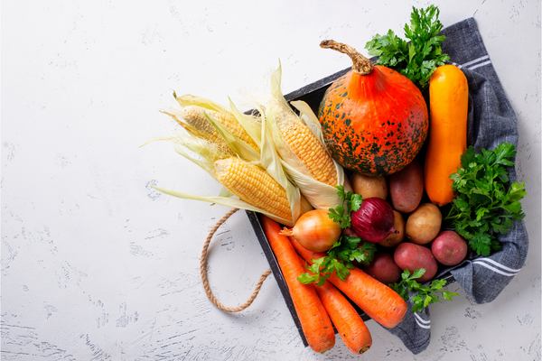 vegetables like corn, carrots and squash and other items in a vegan diet in a wooden box