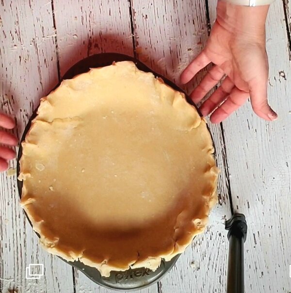image of a vegan pie crust in a metal pie plate with two hands around it