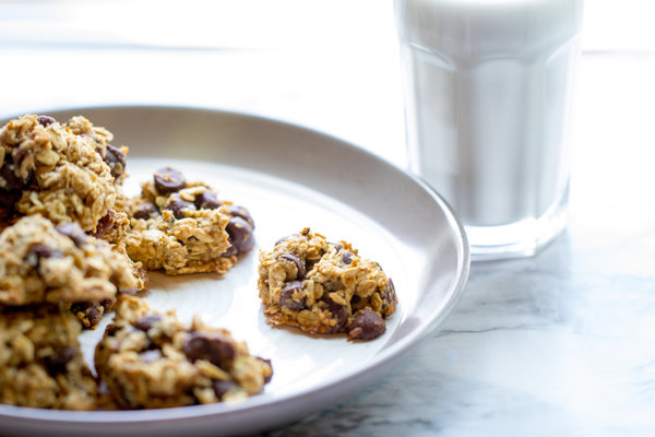 image of vegan oatmeal cookies on a plate with a glass of plant-based milk in the background
