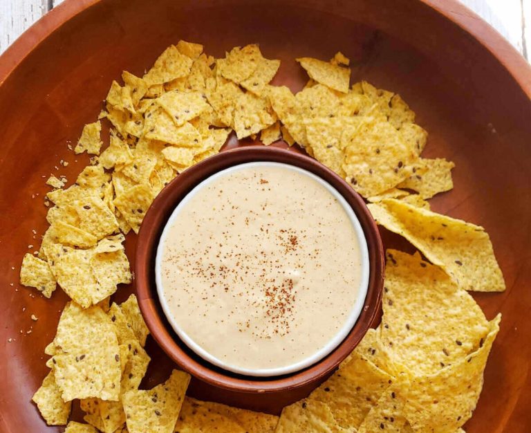 image of easy vegan queso dip in a white bowl surrounded by tortilla chips
