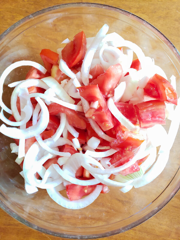 sliced onions and chopped tomatoes in a glass bowl
