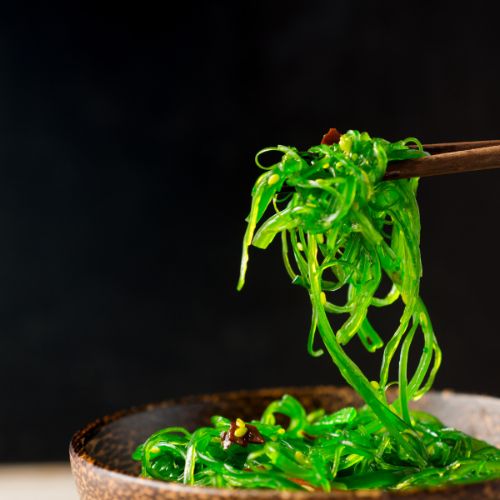 seaweed salad being held over a bowl with chopsticks