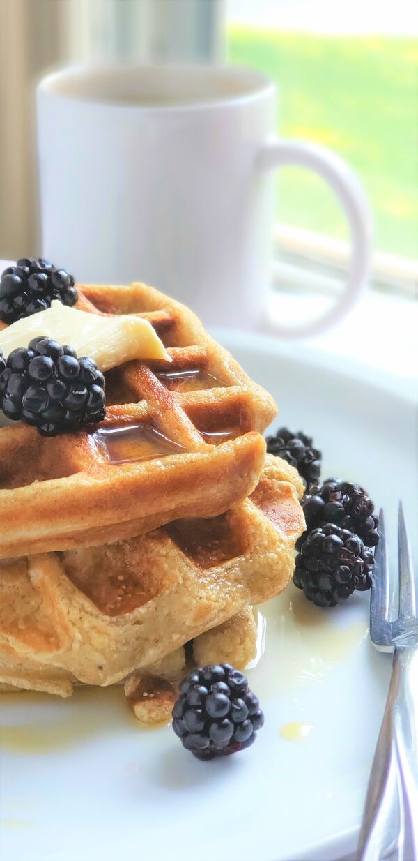 a stack of waffles made with oat flour topped with dairy free butter and blackberries