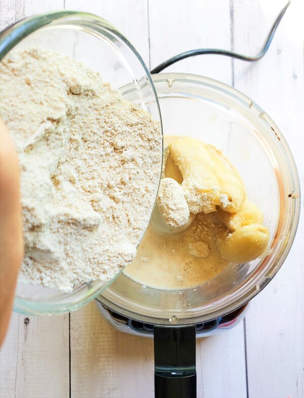oat flour being added to a food processor with bananas and non dairy milk