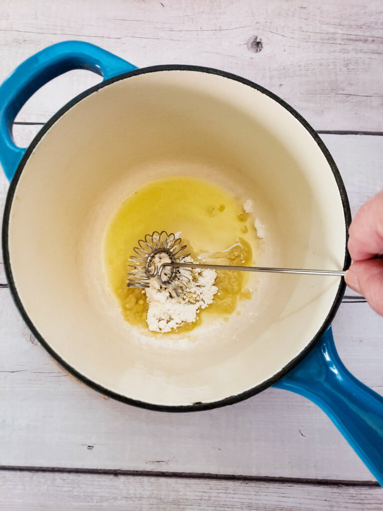 saucepan with oil and flour being mixed with a whisk