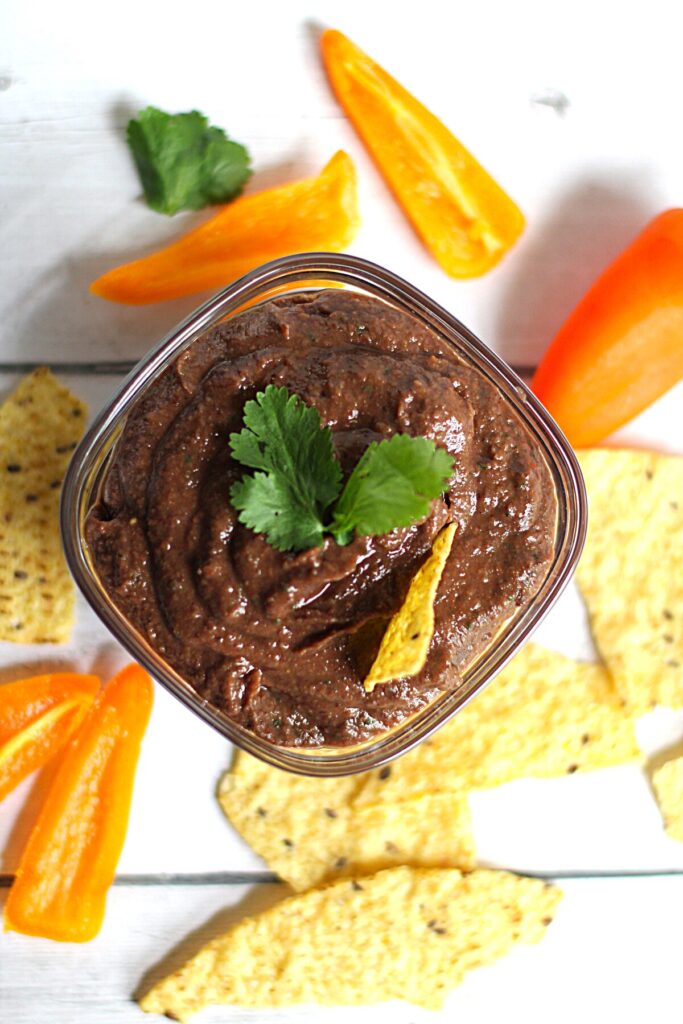 vegan black bean dip in glass bowl with tortilla chips and peppers