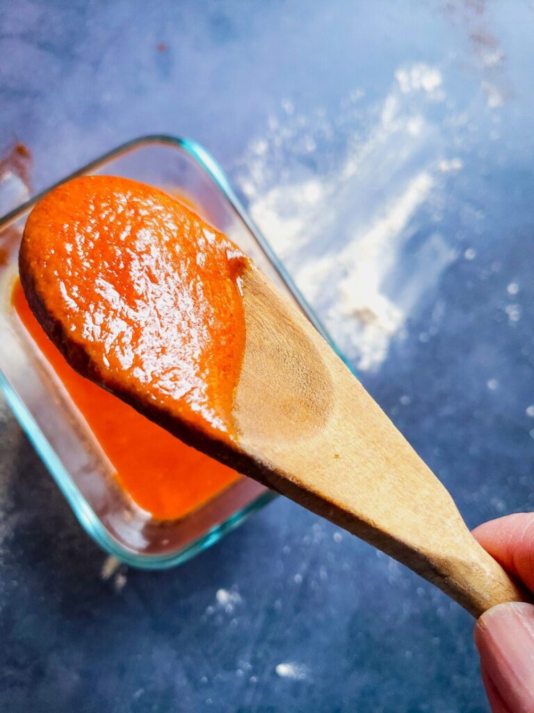 enchilada sauce on a wooden spoon being held over a glass bowl