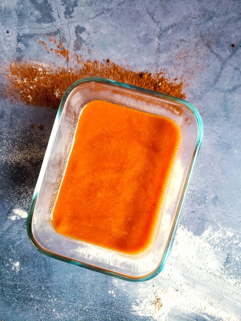 enchilada sauce in a glass bowl surrounded by spices