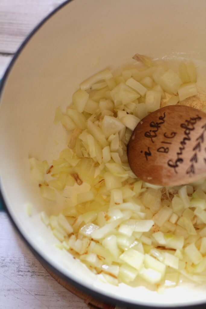 Sauteed onions and garlic in a saucepan with a wooden spoon