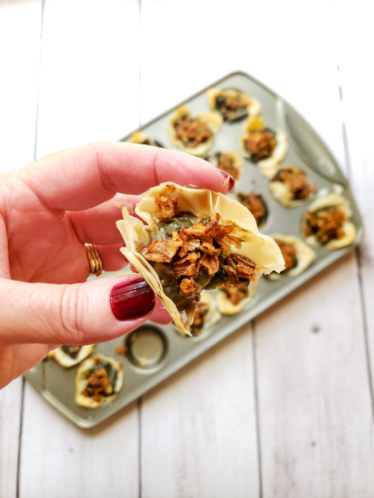 green bean appetizers in a mini muffin tin with a hand holding one