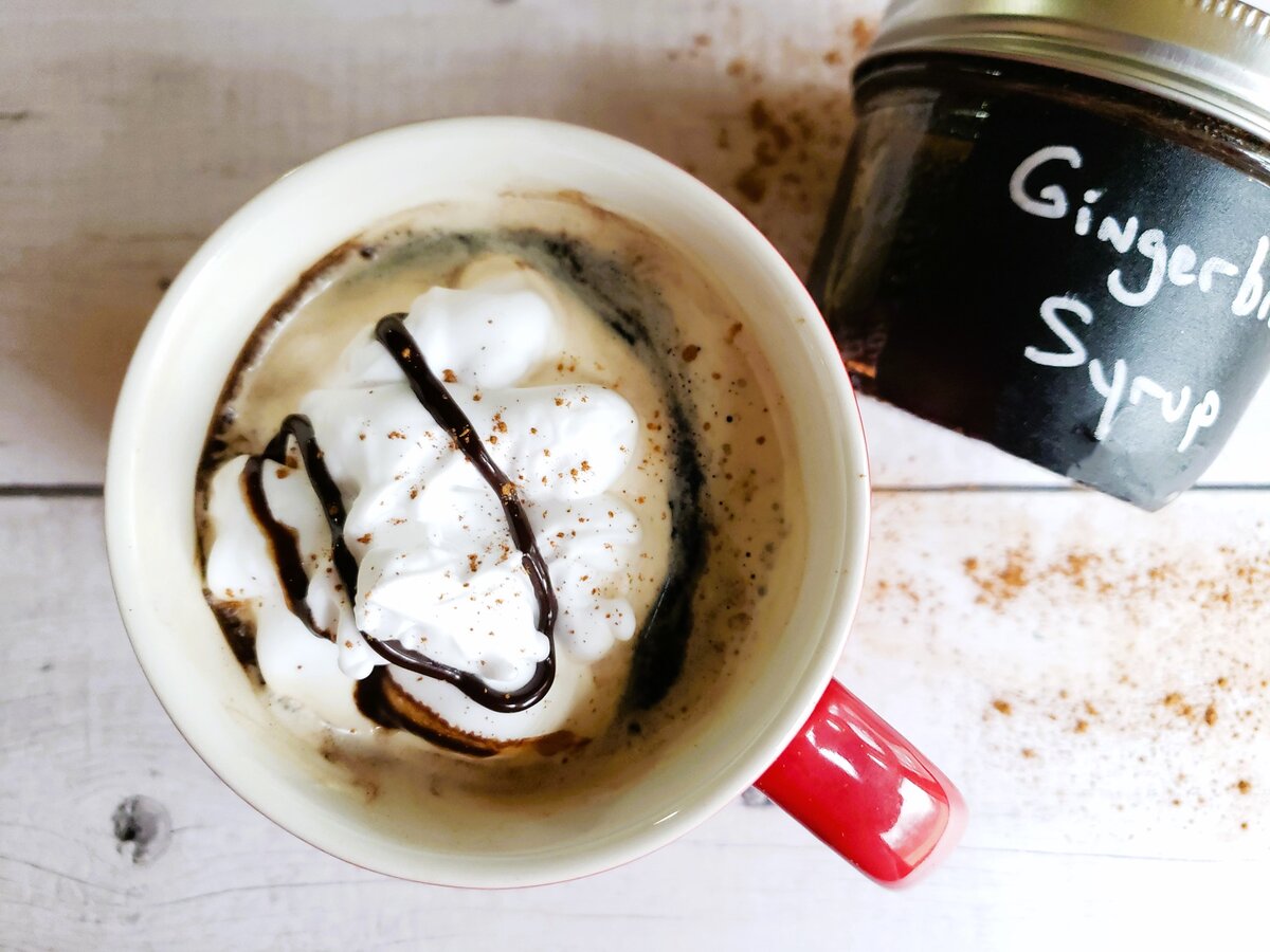 cup of gingerbread latte starbucks recipe with whipped cream and chocolate drizzle next to jar of gingerbread syrup