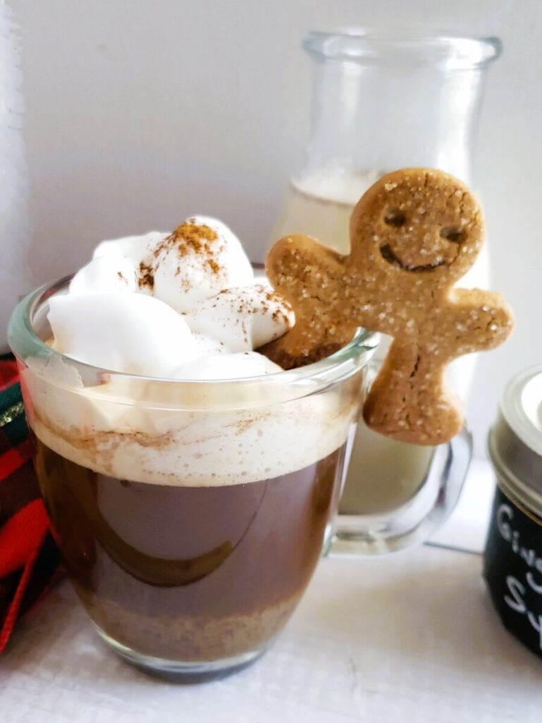 gingerbread latte in a clear glass mug with whipped cream and gingerbread man cookie