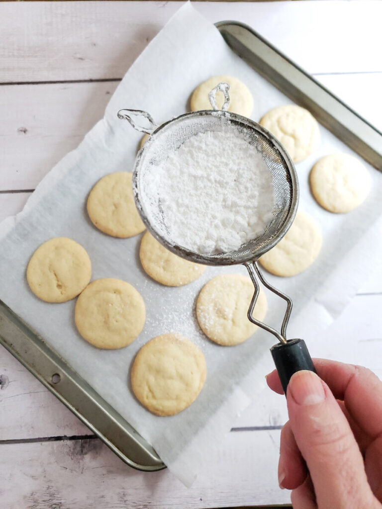 basic vegan cookies on a cookie sheet with powdered sugar being sprinkled over them.