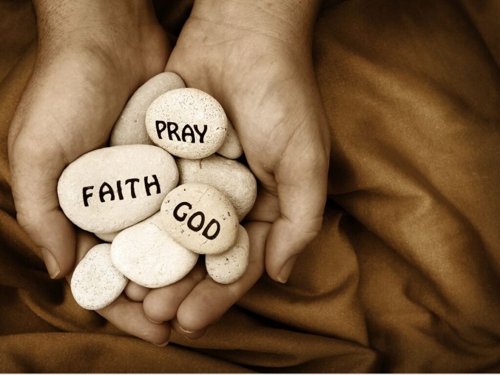 hands holding stones that say faith, pray, God