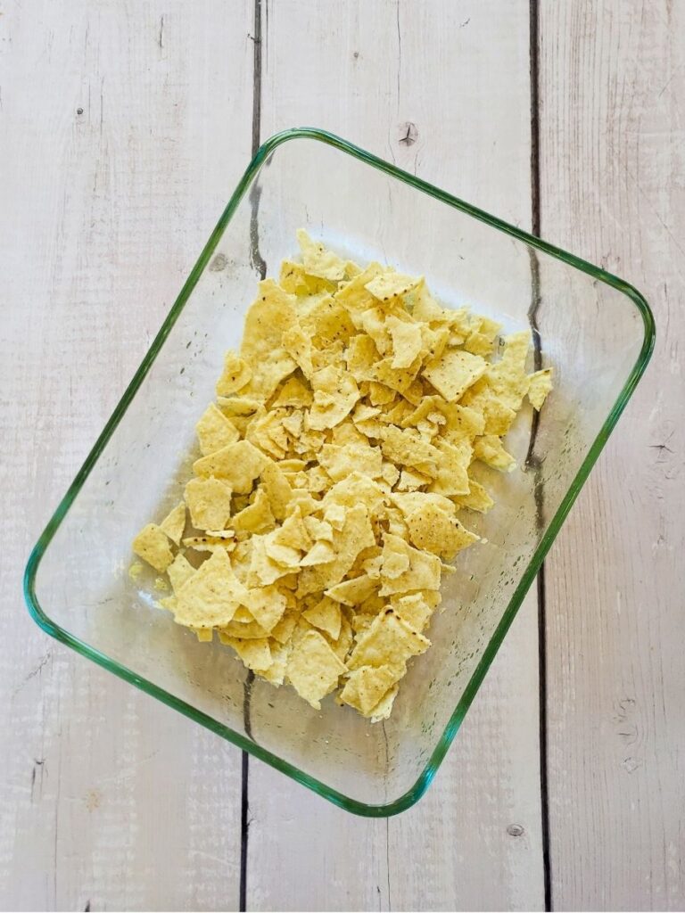 broken tortilla chips in the bottom of a greased casserole dish