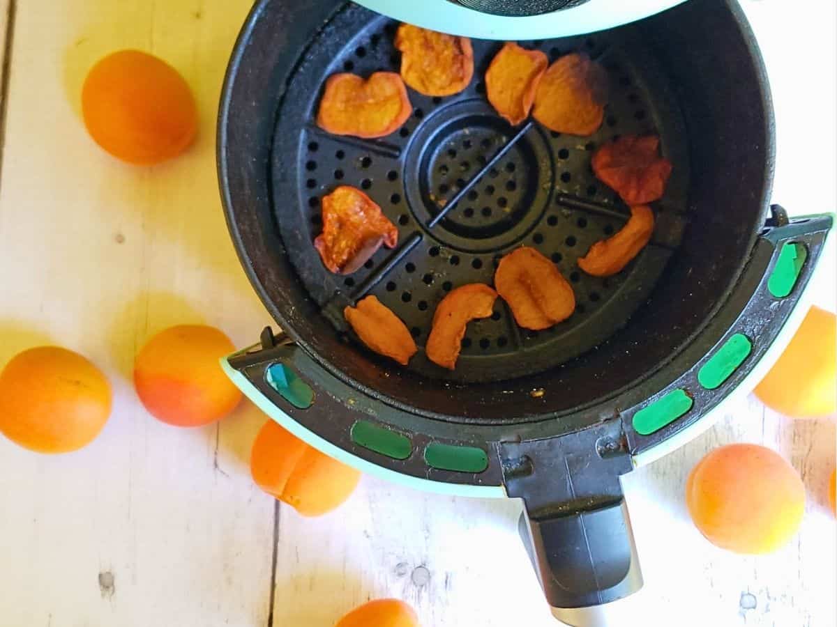 dried apricots in air fryer basket surrounded by fresh apricots
