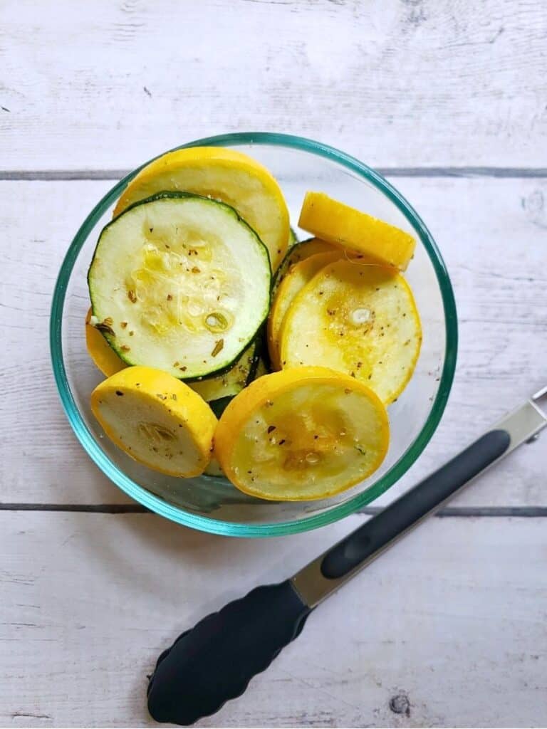 zucchini and squash in a glass bowl with tongs
