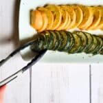 roasted zucchini and squash on a white plate with a hand and tongs