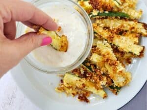 a hand dipping fried zucchini into dairy free ranch dressing